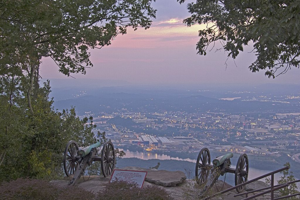 Two canons sit on the edge of a lookout surrounded by trees, with a view of the city.